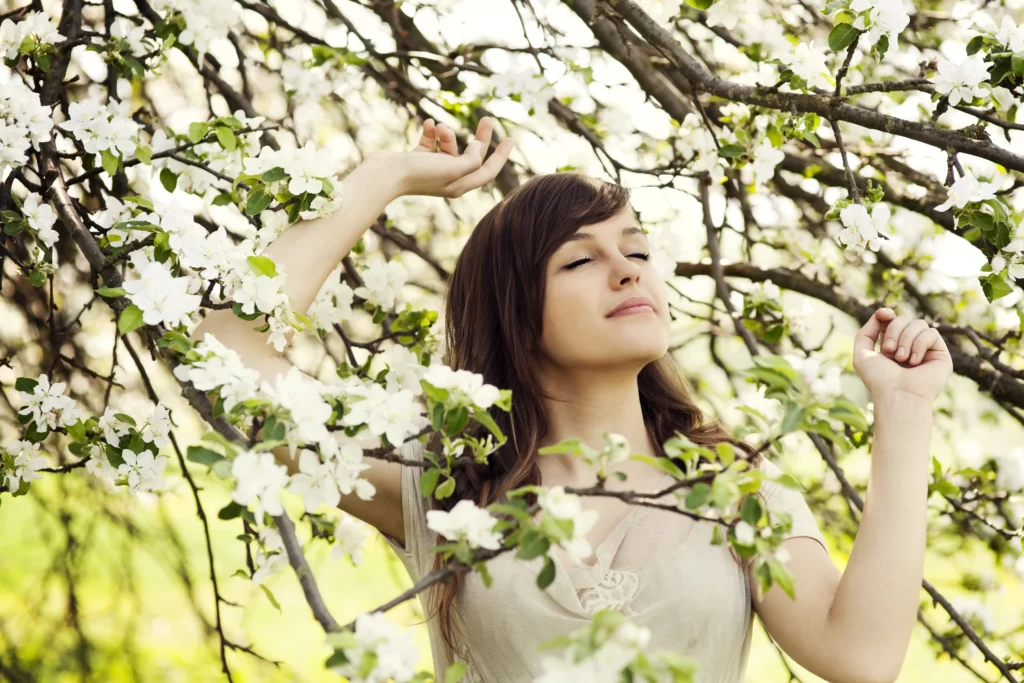 فردی که در بین شکوفه درختان قرار دارد و چشمان خود را بسته است و دستان خود را بالا برده است