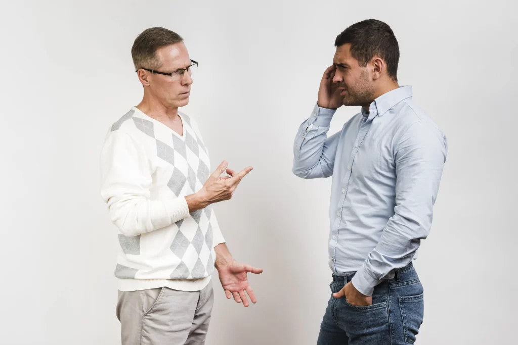 این عکس دو مرد را نشان می‌دهد که در کنار یکدیگر ایستاده‌اند و در گفتگویی مشغول هستند. یکی از مردها عینک و سویشرت پوشیده، در حالی که مرد دیگر یک تلفن همراه را در گوش خود نگه داشته است. هر دو مرد به نظر می‌رسند در بحث فعالانه‌ای شرکت می‌کنند و ممکن است مرد سمت چپ به چیزی اشاره کند. صحنه‌ای از تعامل غیررسمی و دوستانه بین دو فرد را نشان می‌دهد.