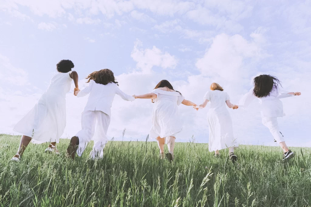 5 تا دختر که در زمین سبزی قرار دارند و دستان همدیگر را گرفته اند و درحال دویدن هستند