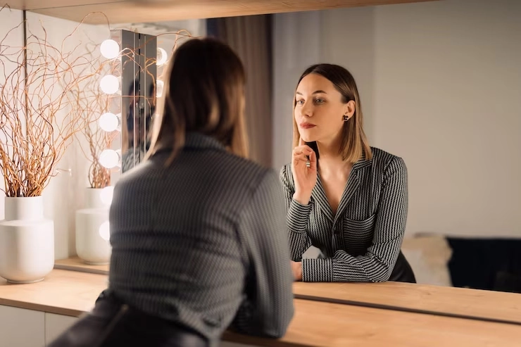 زن جوان ایستاده روبروی آینه در حال نگاه کردن به خود
